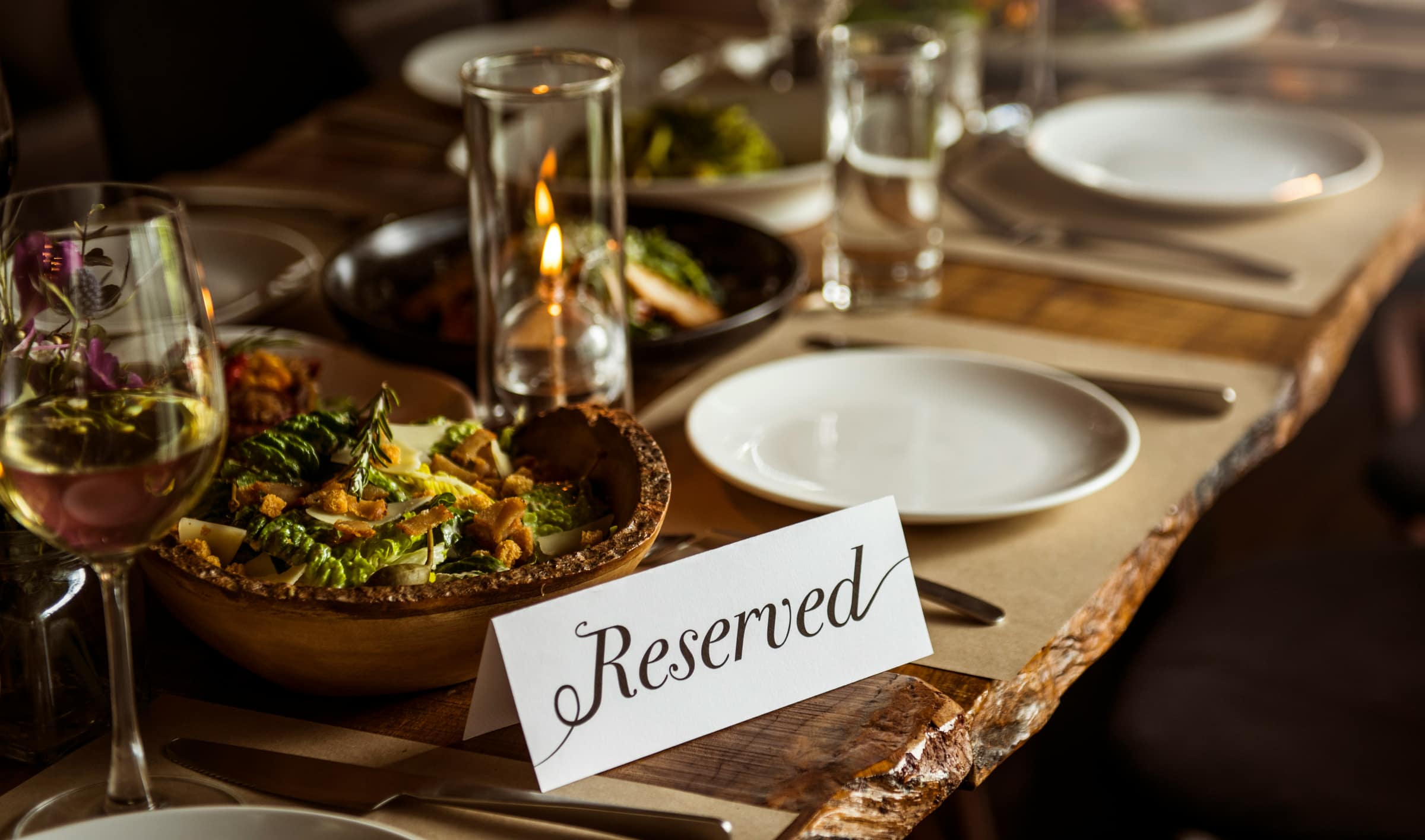 A long table set for a group in warm evening light, with wine glasses, shared dishes, and a Reserved card